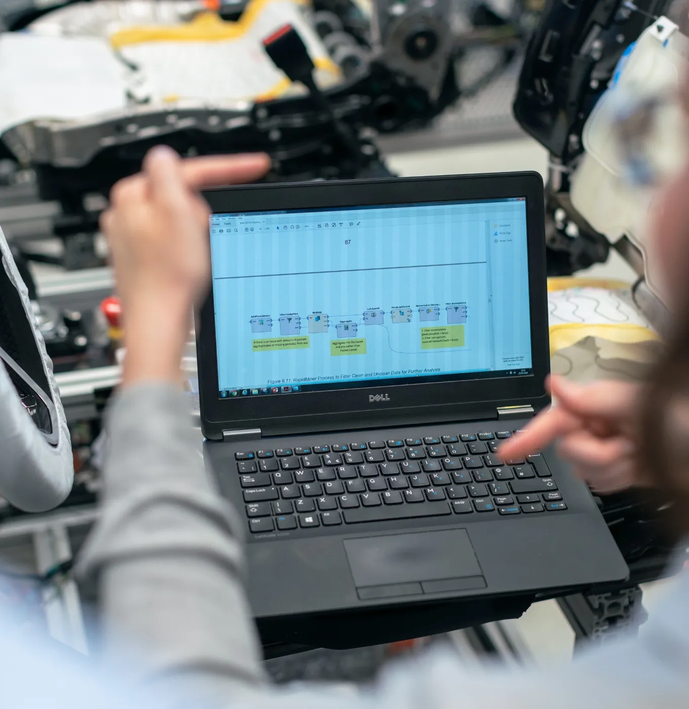 Person pointing at a laptop screen displaying a data flow diagram inside an industrial setting.